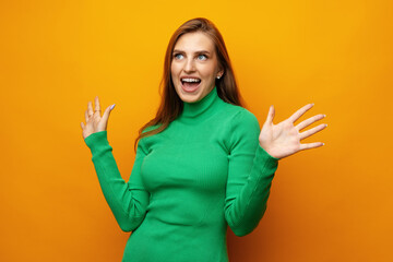 Young pretty surprised smiling woman standing with open palms on yellow background