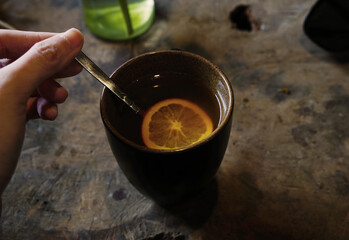 Hand holding a spoon stirring a cup of ginger tea with orange slice - Powered by Adobe