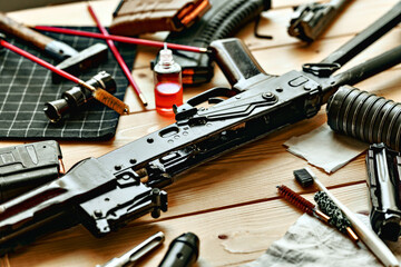 Black disassembled shotgun and cleaning tools on wooden table .