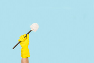 Mano con guante de goma amarillo sosteniendo una escobilla de limpieza sobre un fondo celeste pastel liso y aislado. Vista de frente y de cerca. Copy space - obrazy, fototapety, plakaty