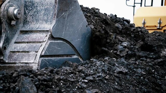 Excavator bucket scoops up rocks. Close-up. High contrast image. Clear white sky. The process of working in a quarry. 4K