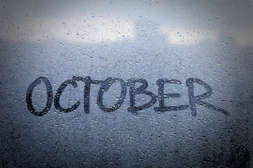 The inscription on the window: October. Finger drawing on the misted glass. Autumn rainy weather