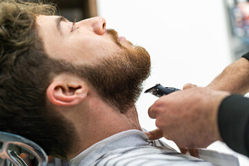 A bearded client of a shaving salon has his beard trimmed with a clipper