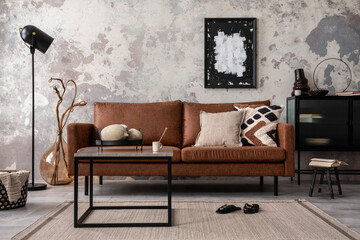 Interior design of loft industrial apartment with mock up poster frame, modern brown sofa, square coffee table,  commode and stylish personal accessories. Concrete gray wall. Home decor. Template