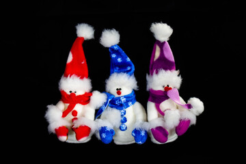 Three handmade toy snowmen with hats and scarves on a black background. Made of felt, scarf, black button, close up. Decor. Christmas and New Year concept