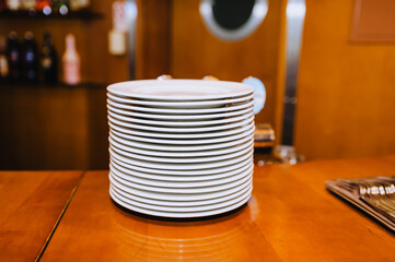 A lot of white clean empty plates stand in a row on a wooden table in the kitchen.
