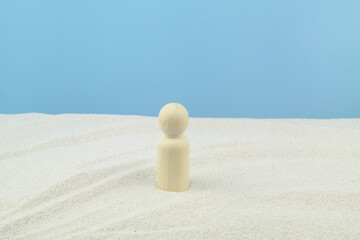 One wooden human figure alone on sand against blue background. Concept of loneliness and surviving. 