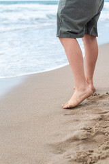 Bare feet of a teenage boy on the sandy shore at the edge of the surf