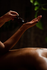 Girl enjoying therapeutic massage with oil in spa with dark lighting, closeup