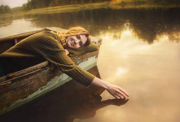 A beautiful blonde woman in a vintage sweater lies in an old fishing boat and touches the surface...