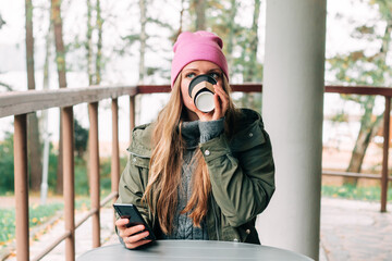 Young woman sitting on outdoor terrace in the forest drinking a cup of hot coffee. Beautiful female relax and enjoy outdoor activity lifestyle in nature on autumn travel vacation