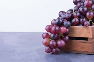 Bunches of fresh ripe red grapes on a wooden textural surface. Ancient style, a beautiful background with a branch of black grape. Red grapes in a box on a stone table, purple grapes, side viwe.