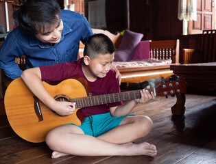 Asian family handsome happy father and son playing guitar together, father teaching son how to play...