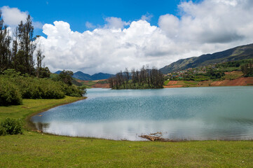 Towering mountains, river with visible small island, blue and white sky, reflection visible in water, nature's gift of greenery everywhere is the way one can explain the beauty of Ooty.