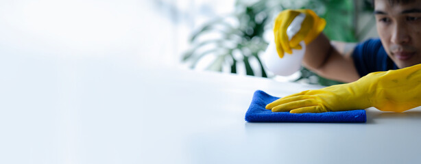 Person cleaning the room, cleaning staff is using cloth and spraying disinfectant to wipe the...