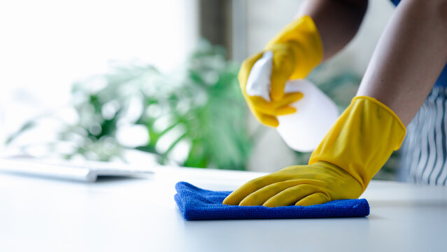Person cleaning the room, cleaning staff is using cloth and spraying disinfectant to wipe the tables in the company office room. Cleaning staff. Maintaining cleanliness in the organization.