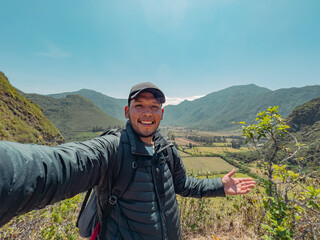 Cheerful ethnic guy taking selfie against mountainous terrain under blue sky