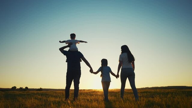 people in the park. happy family walking silhouette at sunset. mom dad and daughters walk holding hands in the park. happy family childhood dream sun concept. parents and children go back silhouette