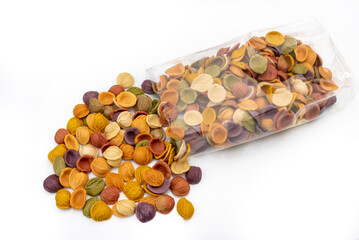 Colored pasta orecchiette that come out of transparent bag, italian durum wheat semolina pasta with turmeric, spinach, beetroot and black carrot isolated on white