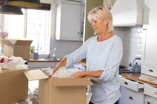 Happy senior caucasian woman moving house, unpacking boxes in kitchen
