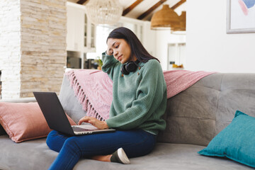 Happy biracial woman sitting on sofa in living room, using laptop