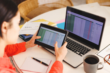 Biracial woman sitting at table in kitchen, using laptop and tablet