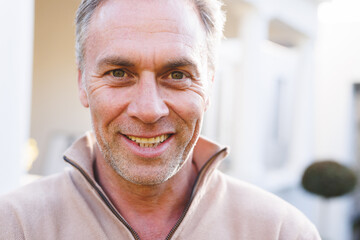 Portrait of happy caucasian man standing outside house and looking at camera