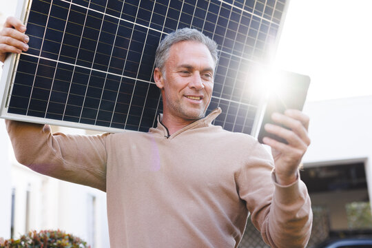 Happy caucasian using smartphone and golding solar panel outside the house