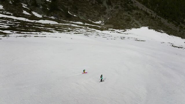 Two skiers ride at high speed down the gorge on the snow between the grass. aerial view