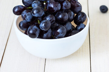 Bunches of fresh ripe black grapes on a wooden textural surface. Ancient style, a beautiful background with a branch of black grape. black grapes in bowl on wooden table, purple grapes, top view.