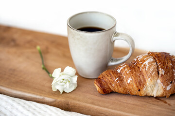 Cup of morning coffee and chocolate croissant on wooden tray in bed