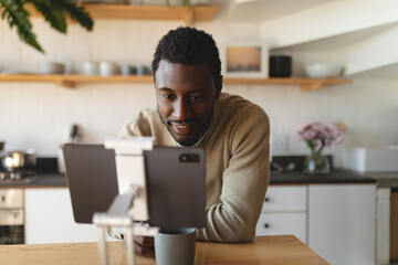 Happy african american man leaning on countertop and using tablet in kitchen