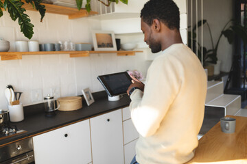 Happy african american man leaning on countertop and using tablet in kitchen