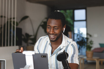 Happy african american man sitting at table in kitchen using tablet for video call