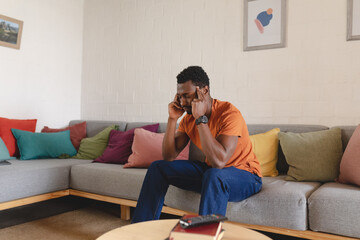 Thoughtful african american man sitting on sofa in living room, holding his head