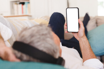 Caucasian man laying on sofa in living room and using smartphone with copyspace