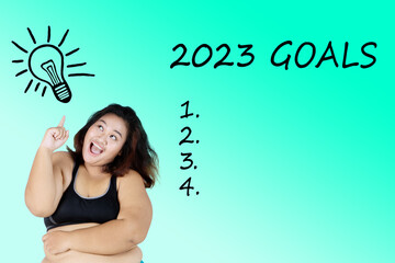 Fat woman standing with 2023 goals list on studio