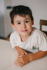 Fototapeta premium Cute school-age boy sitting at a table in the kitchen, waiting for food, enjoying a happy childhood at home. Healthy eating. Happy family, childhood. People
