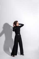 Fototapeta premium Beauty, fashion, style and make-up concept. Beautiful woman with dark pants and blouse studio portrait. Girl making various fashion poses. Model with long dark wavy hair, sun tan and red lipstick 