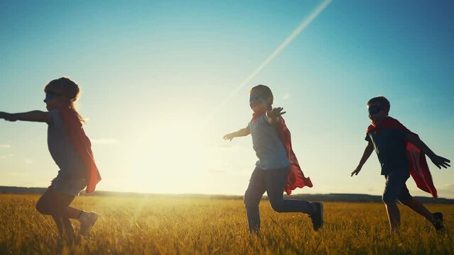 team superhero. a group of children are running across the field in a superhero costume with a silhouette of a red cape at sunset. the concept of a happy family childhood. teamwork dream superhero