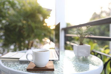 Laptop side view and white coffee cup with notebooks on white glass table outdoor balcony