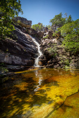 Small waterfall in the middle of the forest with yellowish water in the foreground and blue sky in the background