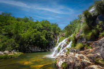 Fototapeta na wymiar Beautiful waterfall among intense vegetation with yellow rocks in the foreground in blue sky day