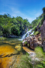Beautiful waterfall among intense vegetation with yellow rocks in the foreground in blue sky day