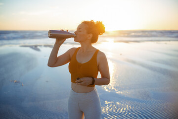 fit sports woman at beach at sundown drinking water