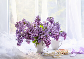 A bouquet of lilacs and a pearl necklace on a light windowsill