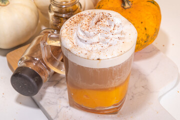 Glass cup with tasty pumpkin spice latte, with white and orange pumpkin squash, pumpkin pie spices and autumn decor copy space. Traditiional autumn Thanksgiving holiday drink