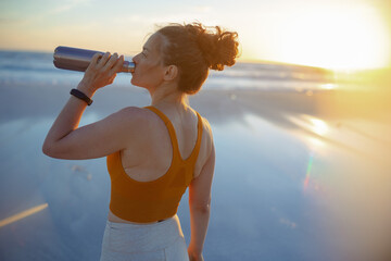 fit sports woman at beach in evening drinking water