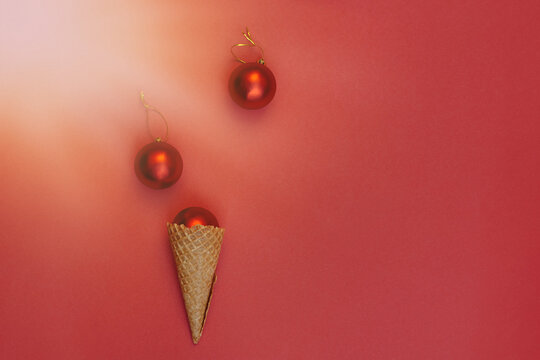 Soft selective focus Christmas balls decoration in waffle cone on red background under bright sun rays. Round toys with gold thread. Flat Lay