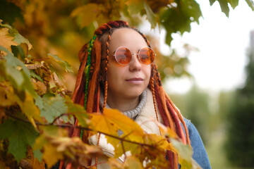 Woman in trendy outfit standing in park. Low angle of young female in casual clothes and trendy sunglasses standing in autumn park